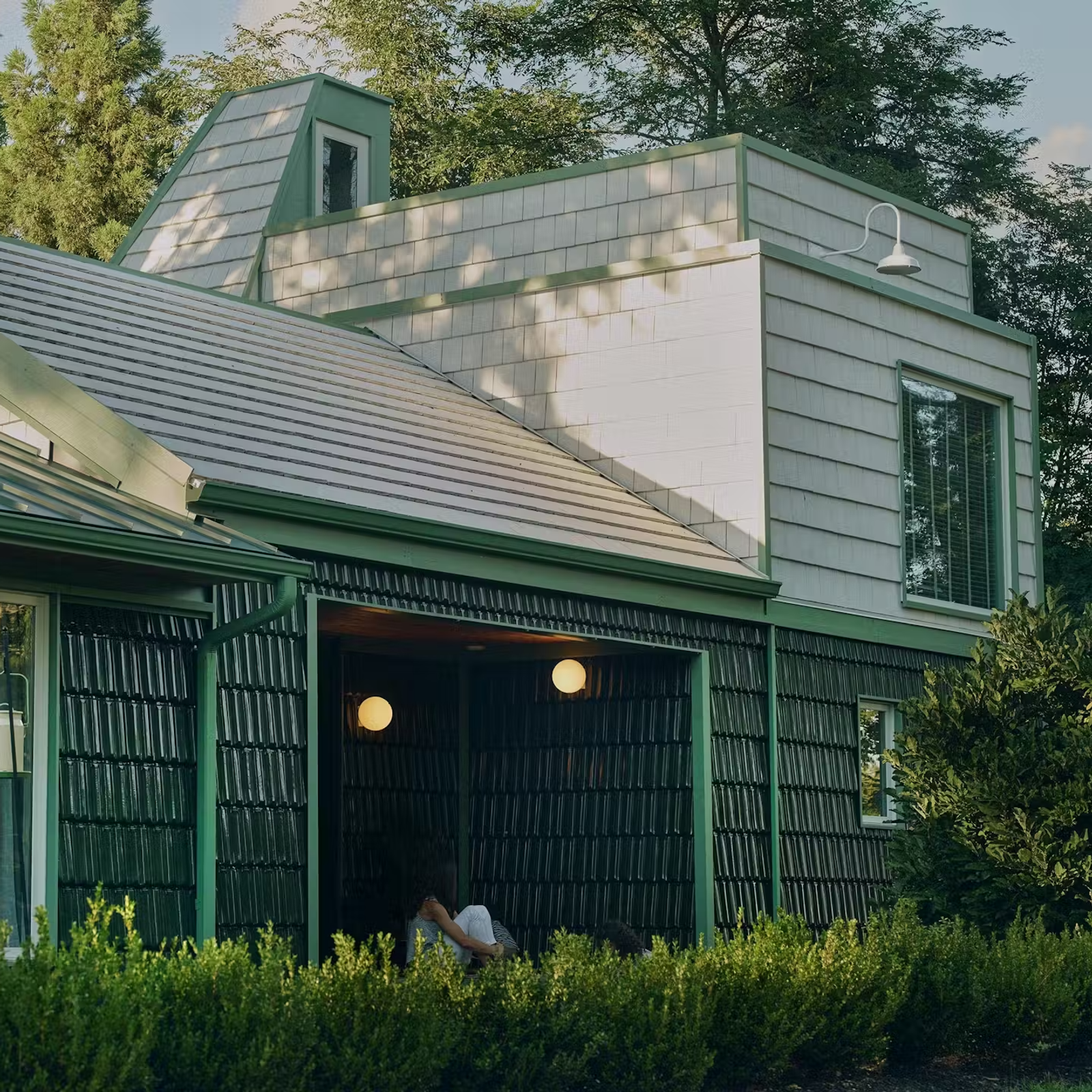 View of addition clad in glazed terracotta French roofing tile, including new entry porch, Dioscuri lights by Artemide. Photograph by Collin Hughes.